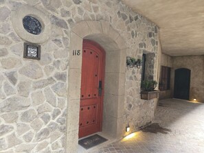 A stone building with a red door, a QR code, and a welcome mat. - Departamento Raziel 118 (Val'Quirico)