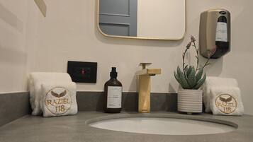 A bathroom with a sink, a hand soap dispenser, a towel rack with towels, and a potted plant.