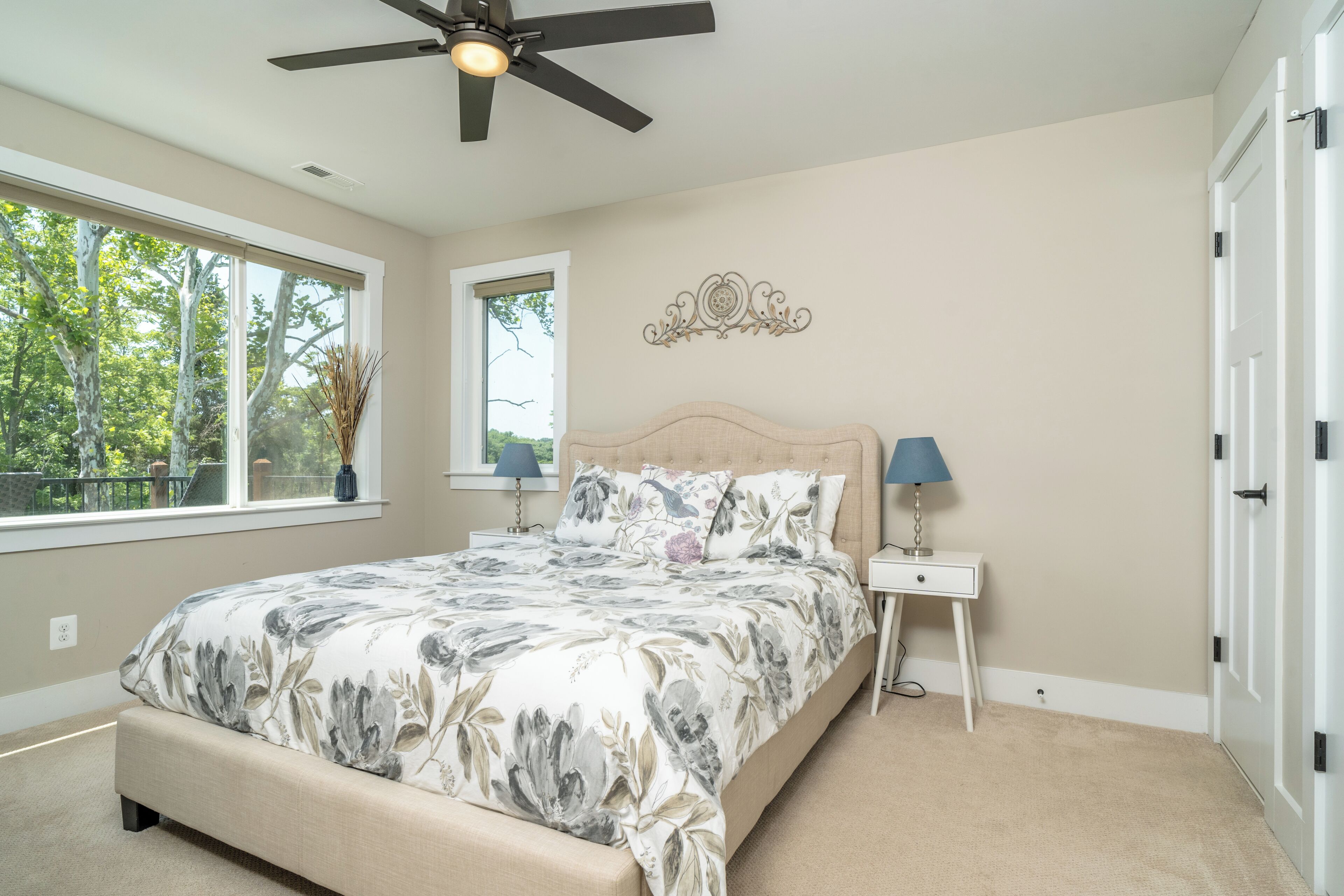 A bedroom with a bed, a ceiling fan, two bedside tables with lamps, a window, and a door.