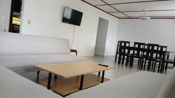 Un soggiorno moderno con un divano, un tavolino in legno, una TV a parete e un'area pranzo con sedie.