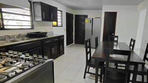 Una cucina con piano cottura a gas, pensili neri, un tavolo da pranzo con sedie e un frigorifero.