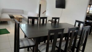 A dining area with a rectangular table and six chairs, a sofa, and a TV mounted on the wall.