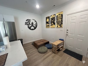 A room with a white countertop, a wooden bench, a small table with shoes, a door, and wall art.