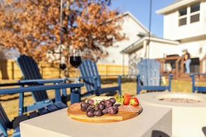Un espace extérieur aménagé avec des chaises bleues et une table sur laquelle est disposée une planche de charcuterie.