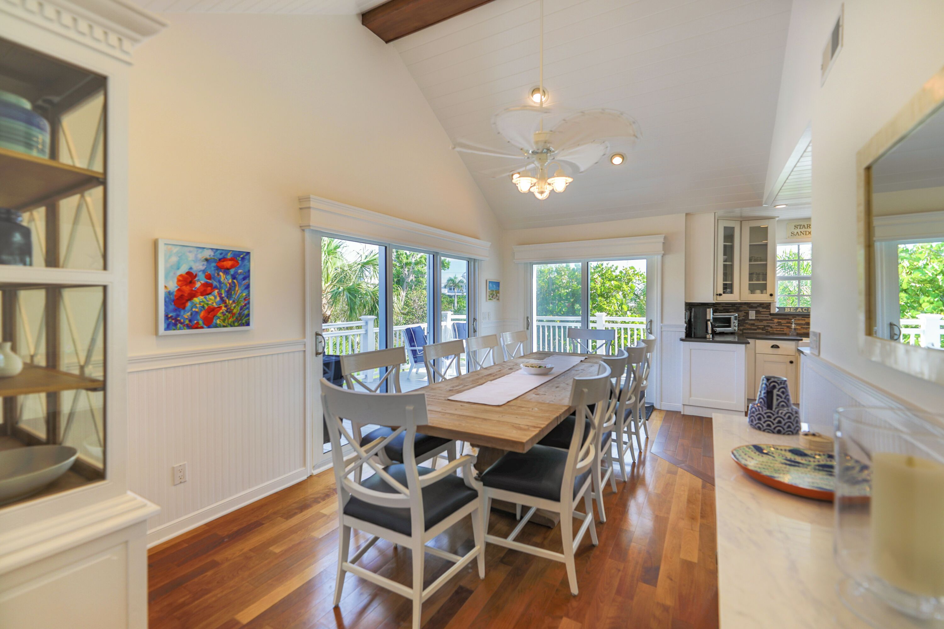 A dining area with a wooden table, white chairs, and a ceiling fan.