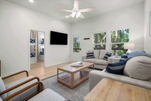 A modern living room with a ceiling fan, a sofa, a coffee table, and a TV mounted on the wall.