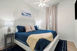 A bedroom with a bed, nightstand, lamp, ceiling fan, and a painting on the wall.