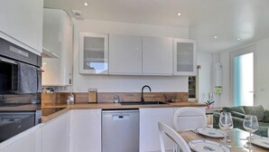 Uma cozinha moderna com armários brancos, máquina de lavar louça e um espaço de jantar com mesa posta para dois.