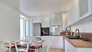 Cozinha moderna com armários brancos, bancada de madeira e área de refeições com cadeiras brancas e mesa de vidro.