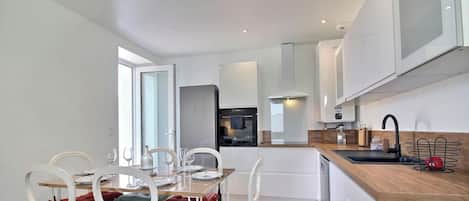 A modern kitchen with white cabinetry, a wooden countertop, and a dining area with white chairs and a glass table.