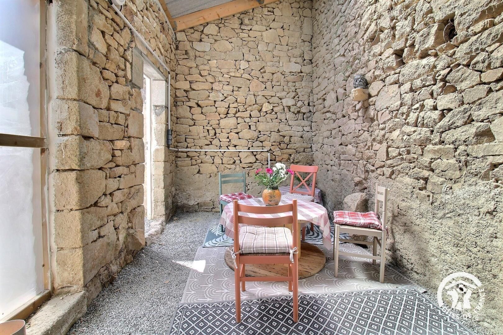 Una habitación con paredes de piedra, una mesa, sillas, una ventana y una puerta.