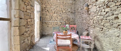 A stone-walled room with a table and chairs, a window, and a door.