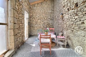 Ein Zimmer mit Steinwänden, einem Tisch, Stühlen, einem Fenster und einer Tür.