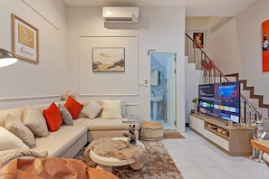 A living room with a sofa, a television, a coffee table, and a staircase leading to a bathroom. - Coco's Townhouse BTS Onnut 350 Meters 3br3bth (Bangkok)