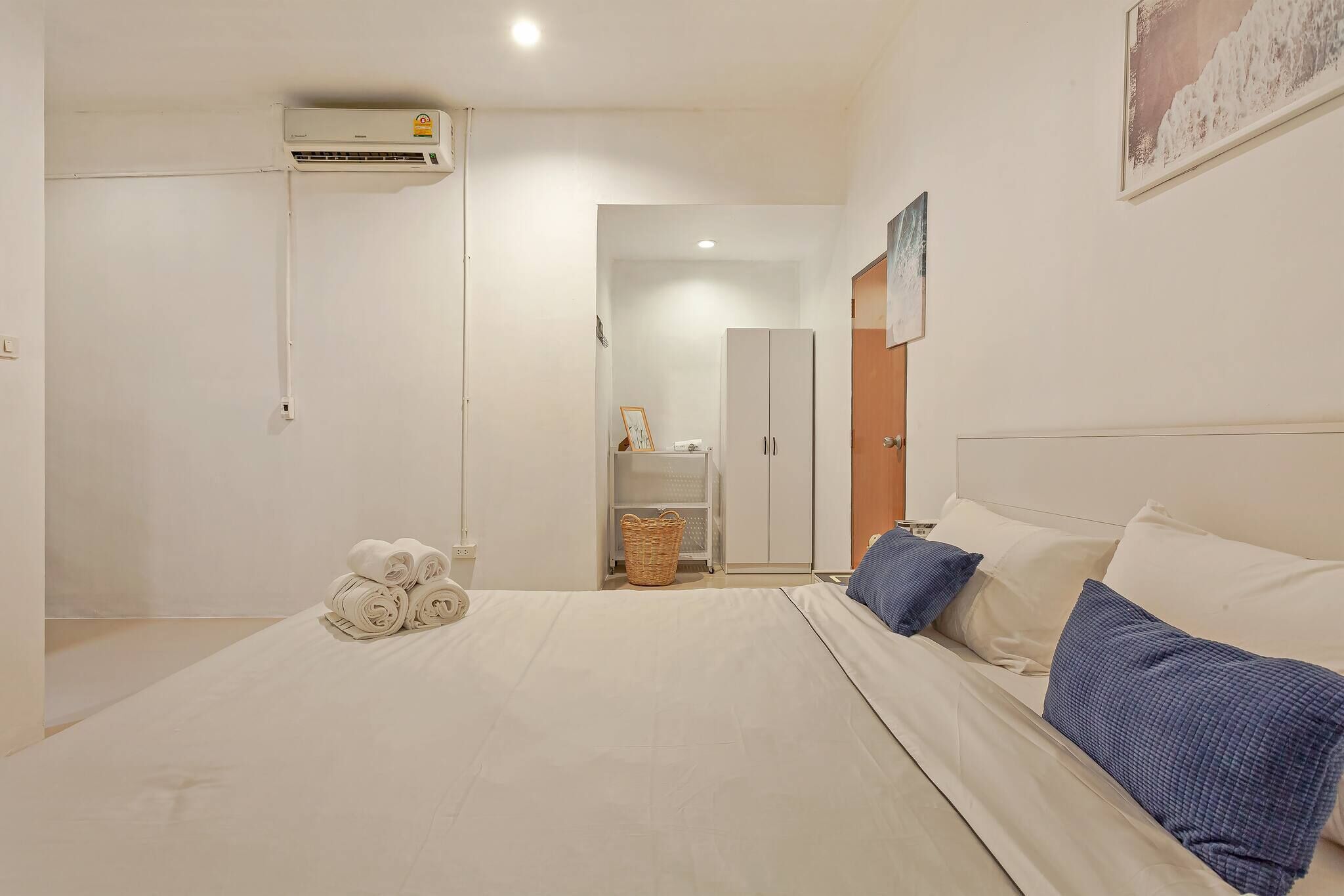 A bedroom with a bed, pillows, a basket, a wardrobe, and an air conditioning unit.