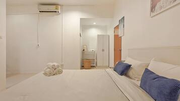 A bedroom with a bed, pillows, a basket, a wardrobe, and an air conditioning unit.