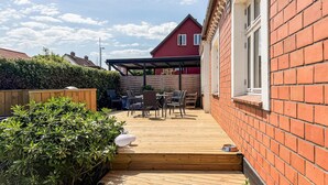 A wooden deck leading to a covered outdoor seating area with a brick house in the background. - Amazing home in Allinge with WiFi (Allinge)