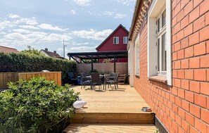A wooden deck leading to a covered outdoor seating area with a brick house in the background. - Amazing home in Allinge with WiFi (Allinge)