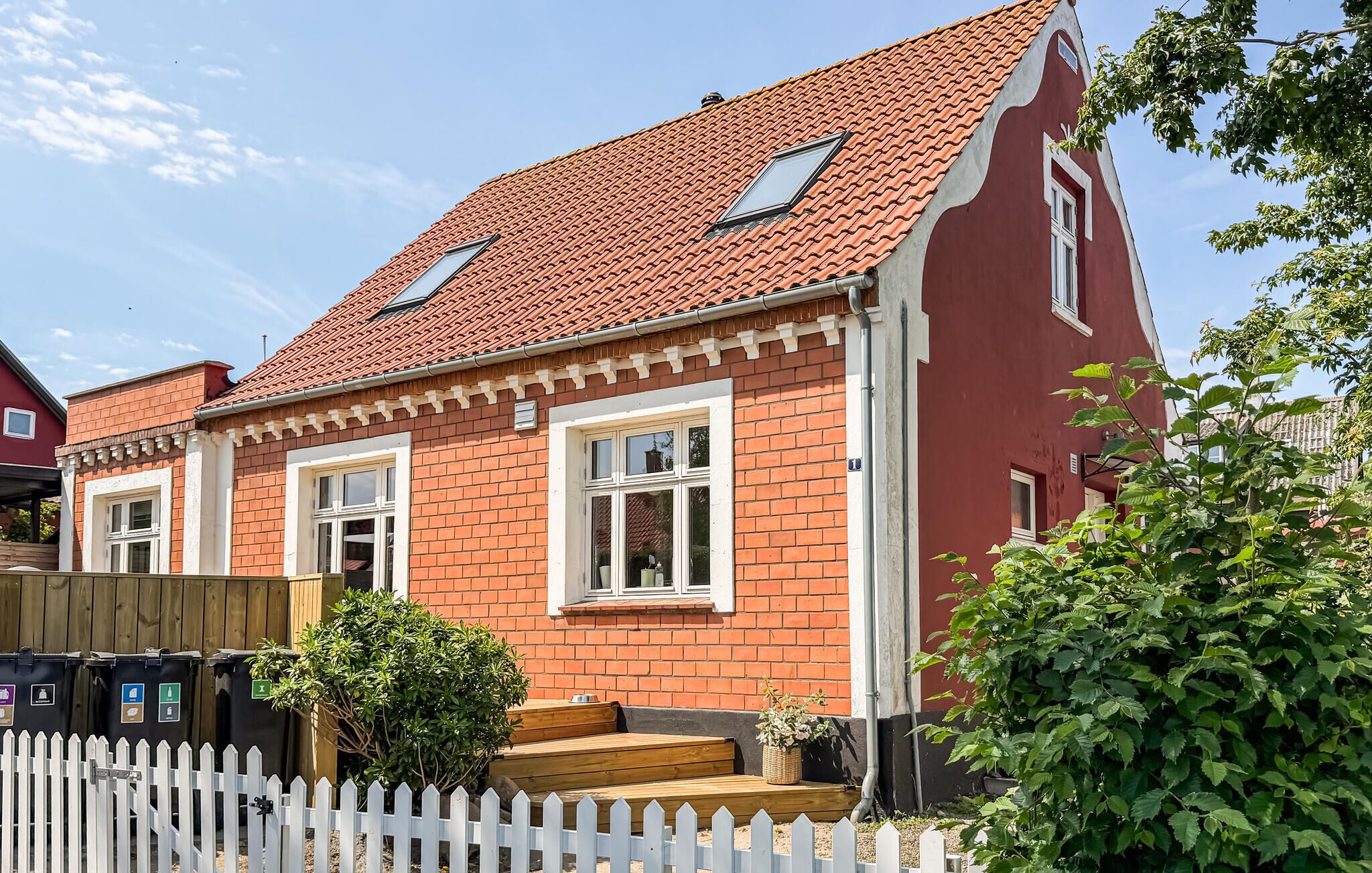 Ein rotes Backsteinhaus mit zwei Fenstern, einem weißen Zaun und einem kleinen Garten.