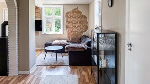 A living room with a brick wall, a sofa, a glass cabinet with wine glasses, and a television. - Amazing home in Allinge with WiFi (Allinge)