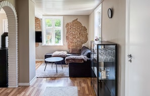 A living room with a brick wall, a sofa, a glass cabinet with wine glasses, and a television. - Amazing home in Allinge with WiFi (Allinge)