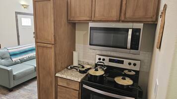 Une cuisine compacte avec des meubles en bois, un four à micro-ondes, une cuisinière avec des casseroles et un petit plan de travail.
