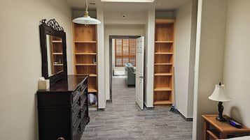 A hotel hallway with a bed, a dresser, a mirror, a ceiling fan, and wooden shelving units.