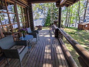 A wooden deck with wicker furniture, a table with a vase of flowers, and a view of a lake.