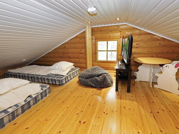 A cozy attic bedroom with a sloped ceiling, a window, a bed, a bean bag, a TV, and a small table.