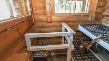 A log cabin interior with a wooden table, a window, and a metal bucket.