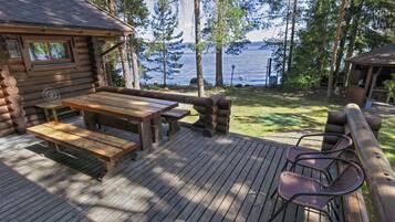 Une cabane en rondins dotée d’une terrasse, d’une table de pique-nique et de chaises, le tout offrant une vue sur un lac.