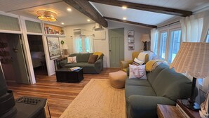 Ein gemütliches Wohnzimmer mit einer Couch, einem Couchtisch und einer Lampe. Ein Bücherregal und eine Tür zu einem anderen Raum sind ebenfalls vorhanden.