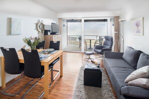 Un salon moderne comprenant un coin repas, un canapé gris, un téléviseur et un balcon avec vue.