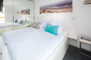 Ein Schlafzimmer mit einem Bett, einem Nachttisch, einem Spiegel und einem an der Wand hängenden Kunstwerk.