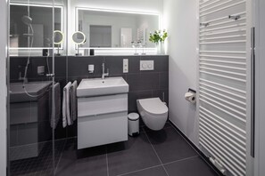 Ein modernes Badezimmer mit Duschkabine aus Glas, einem weißen Waschbecken, einer Toilette und einem Handtuchhalter.