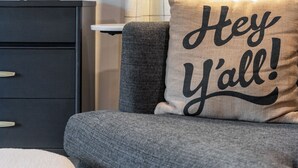 Una sala de estar moderna con un sofá gris, una lámpara decorativa y un cojín con el texto 'Hey y'all!'.