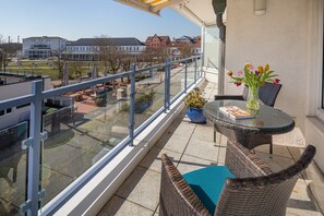 Ein Balkon mit Korbmöbeln, einem Glastisch und einer Blumenvase.