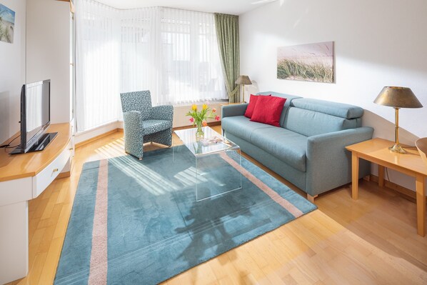 Ein modernes Wohnzimmer mit Sofa, Sessel, Couchtisch, Fernseher, Lampe und Kunstwerken an den Wänden.