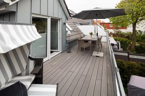 Eine Terrasse mit Tisch und Stühlen, einem gestreiften Sonnenschirm und einer Schiebeglastür.