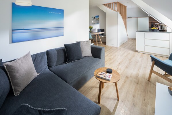 Ein modernes Wohnzimmer mit einer Couch, einem Couchtisch und einer Treppe, die in eine Küche führt.