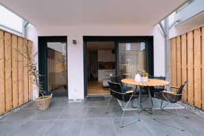 Eine Terrasse mit rundem Tisch und Stühlen, einem Blumentopf und Blick ins Haus.