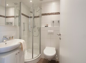 Ein modernes Badezimmer mit einer Duschkabine, einem weißen Waschbecken und einer Toilette.
