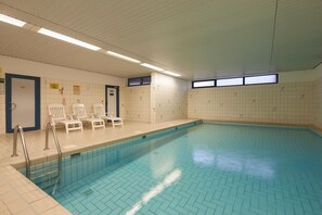 Ein Innenpool mit gefliesten Wänden, einem blauen Beckenboden und weißen Liegestühlen.