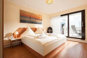 Ein Hotelzimmer mit Bett, Nachttisch mit Lampe, einem Sonnenuntergangsdruck und Blick durch eine Schiebetür nach draußen.