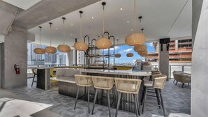 Un espace bar moderne avec des chaises en osier, des luminaires suspendus et une vue sur le paysage urbain.