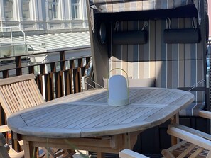 Ein Holztisch im Freien mit Stühlen, ein kleines weißes Objekt auf dem Tisch und eine gestreifte Wand im Hintergrund.