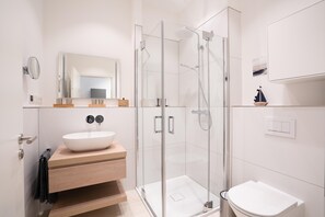 Ein modernes Badezimmer mit einer gläsernen Duschkabine, einem weißen Waschbecken und einem hölzernen Waschtisch.