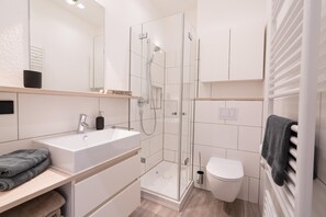 Ein modernes Badezimmer mit Duschkabine aus Glas, einem weißen Waschbecken und einer Toilette.