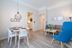 Ein modernes Wohnzimmer mit Essbereich, einem blauen Sessel und einer Couch mit gemusterten Kissen.