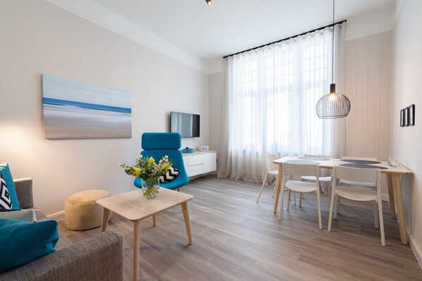 Ein modernes Wohnzimmer mit einer Couch, einem blauen Sessel, einem Esstisch und einem Fernseher.